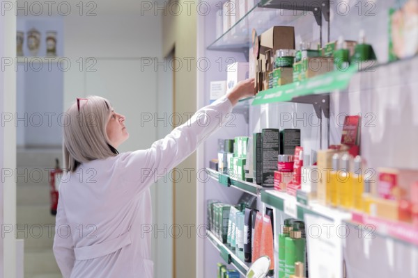 A health professional reviews and organizes a variety of products on the shelves, ensuring quality