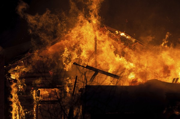 Arson or nature disaster, burning fire flame on wooden house roof