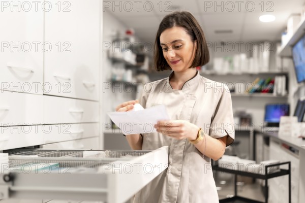 Female young pharmacist looking for medicines in storage compartment in the shop