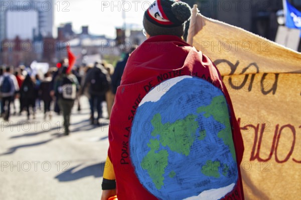 An environmental demonstrator is viewed from behind, marching on a crowded street with during a