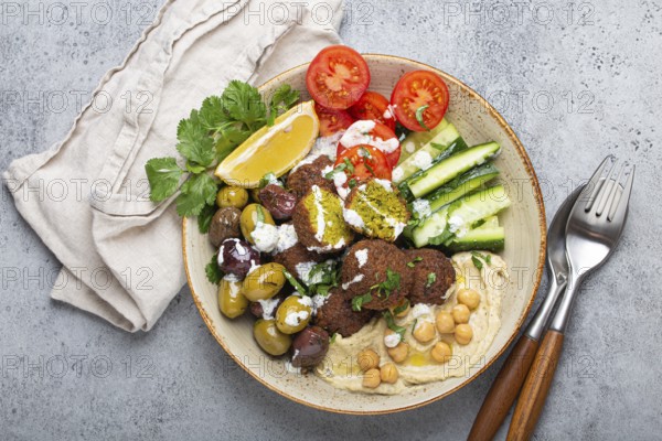Falafel salad bowl with hummus, vegetables, olives, herbs and yogurt sauce. Vegan lunch plate top