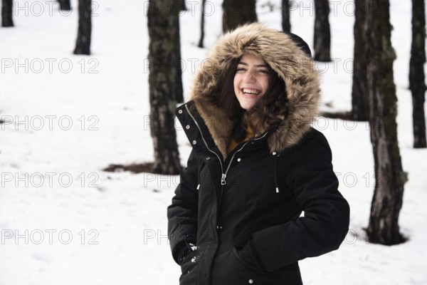 Young happy and beautiful teenage girl dressed in winter clothing standing at snow and smiling.