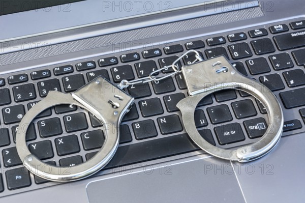 Handcuffs lying on computer keyboard as a symbol for cybercrime
