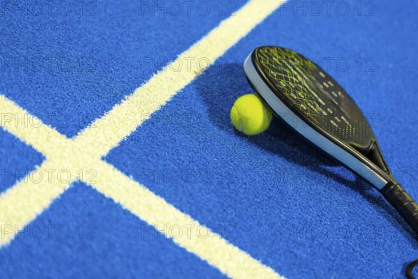 Photo with no people and copy space of a paddle tennis racket leaning on ball in a blue court