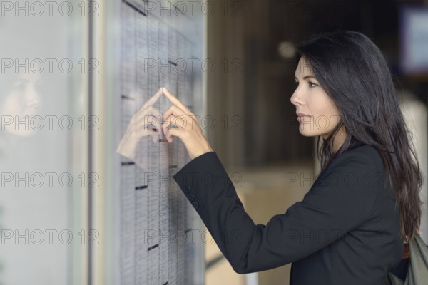Attractive woman reading the train timetable running down the columns with her finger as she tries