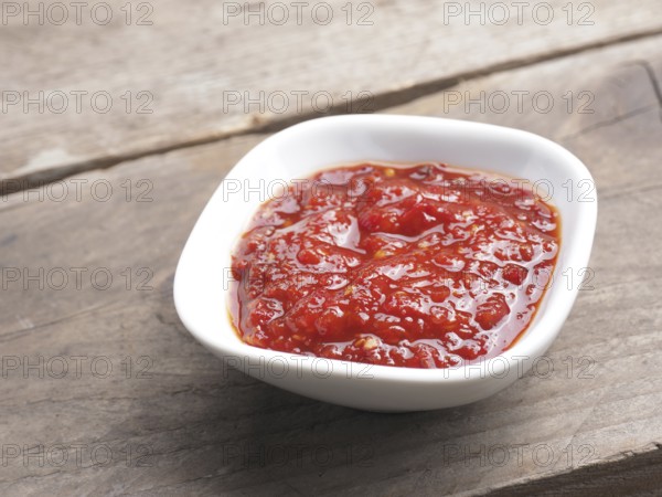 Very spicy chili sauce in a white bowl on a rustic wooden kitchen table, space for your text