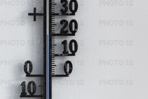 Classic black analog thermometer hanging on white wall displaying blue temperature scale of twenty,