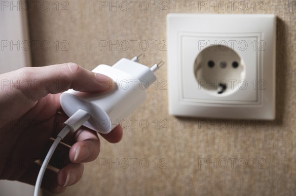 Hand turns on, turns off charger in electrical outlet on wall. White charger for phone in woman's