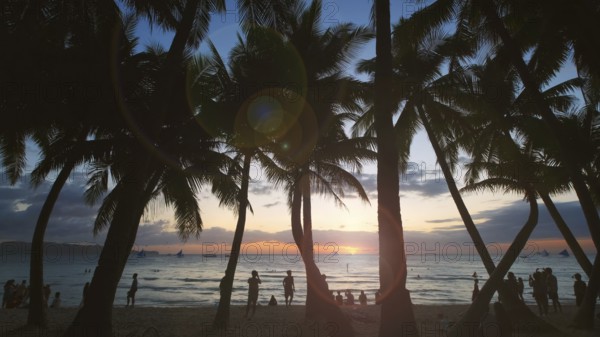 Silhouetted people and palms near sea. Sunset at tropical White beach, Boracay island, Philippines,