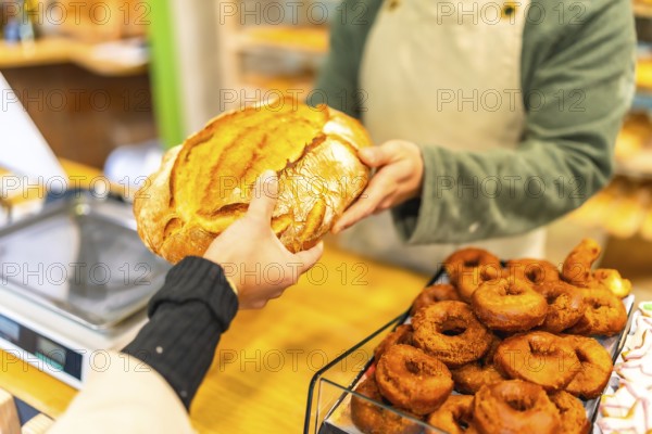 Close-up of the hands of a salesman handing a round artisan bread to a female customer