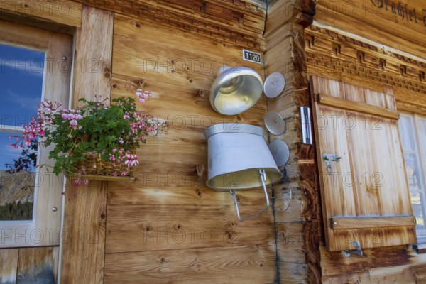 A rustic wooden wall with a window, a flower box and a decorative milk churn, typical alpine