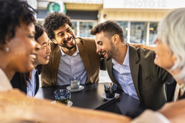 Multi-ethnic business team congratulating and celebrating embracing together sitting in a cafeteria