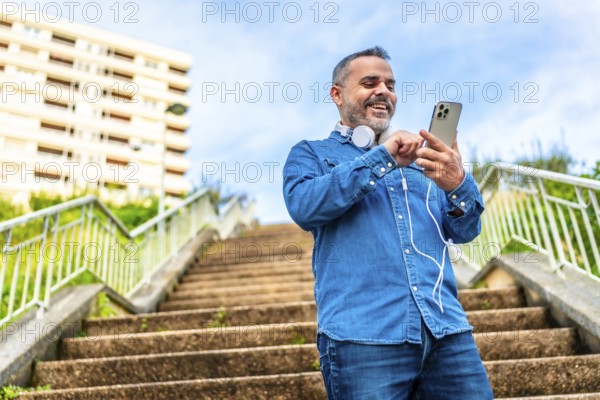 Low angle view photo of a mature man using phone and headphones standing on city stairs
