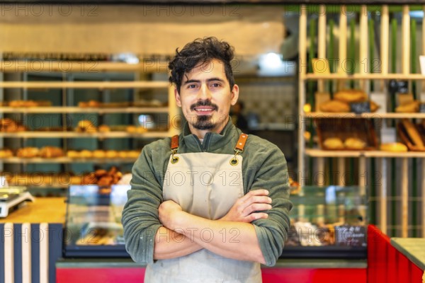 Formal portrait of a latin male young baker standing proud with arms crossed in a modern artisan