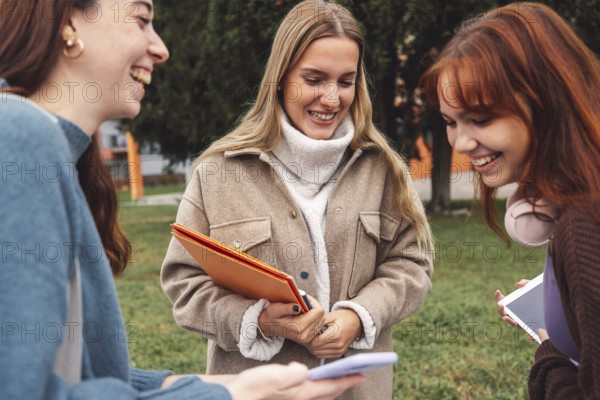Group of three cheerful female collage students outside their dorm on a cold autumn day, walking on
