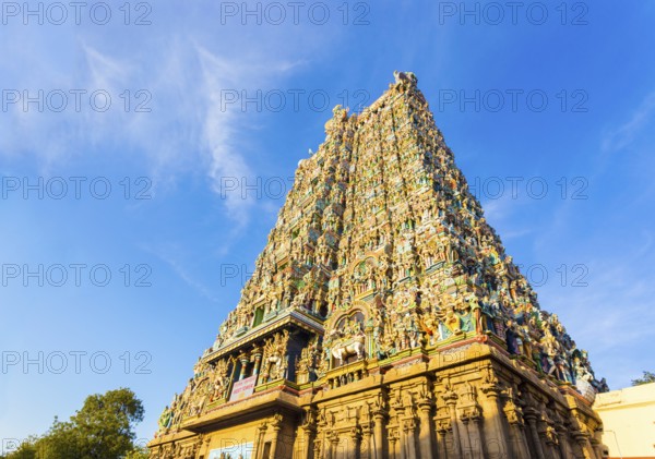 West tower gateway of Meenakshi Amman Temple covered in colorful statues of gods on a blue sky day