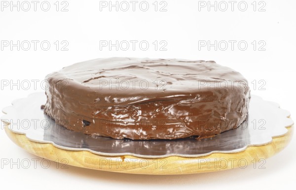 Sacher chocolate cake on a silver plate on wooden board towards white