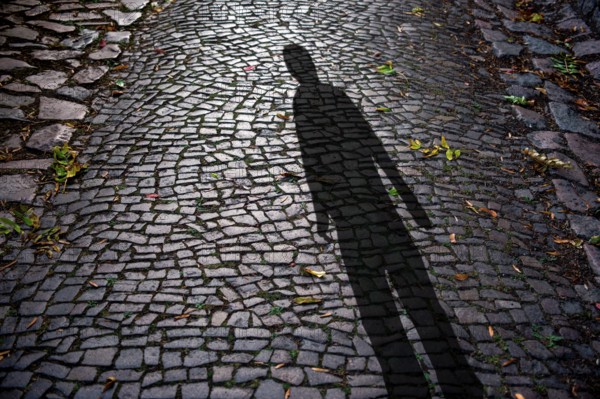 Human shadow on cobblestones at night, symbolic photo crime, burglar, creepy