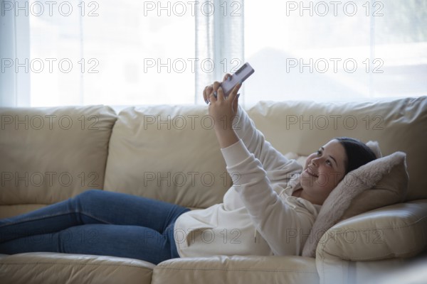 A girl lies comfortably on a sofa, smiling while using her smartphone in a naturally lit room