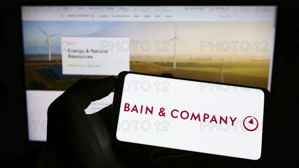 Stuttgart, Germany, 06-11-2022: Person holding cellphone with logo of US consulting company Bain