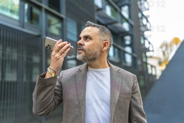 Mature male caucasian businessman sending a voice message in the street next to a financial