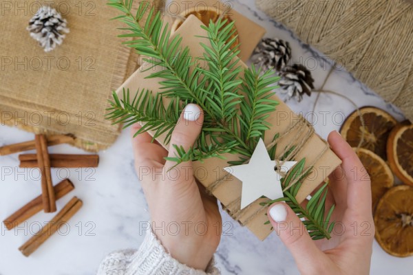 Woman making Box with New Year's gifts, wrapped in craft paper and decorated with fir branch.