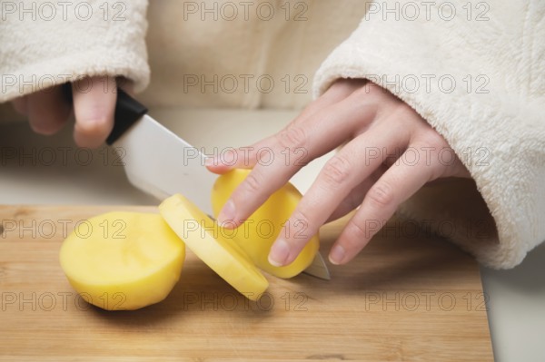 Young caucasian woman in a bathrobe stands in the kitchen and cuts fresh potatoes with a knife, on