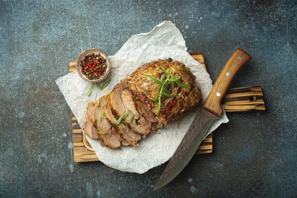 Rolled turkey roasted with spices and herbs on baking paper with knife and rustic concrete
