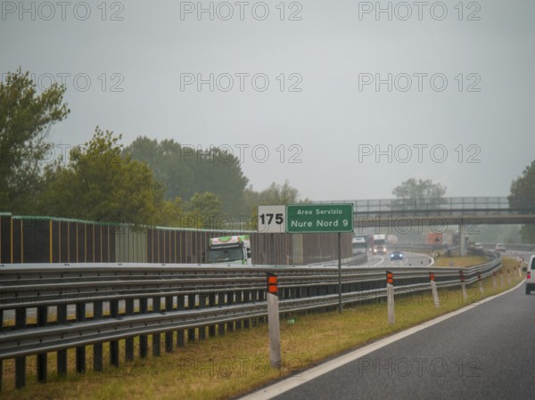 A highway scene under an overcast sky featuring cars and trucks with road signs and an overpass,