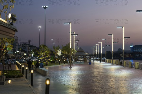 People, locals and tourists stroll and relax on the promenade of the Tapi river in Surat Thani