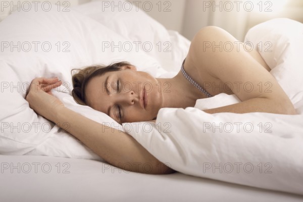Woman sleeping in bed under white quilt with head on pillow