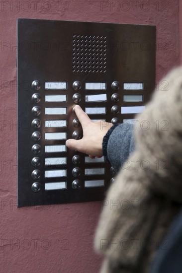 unrecognizable person ringing doorbell at apartment building. many blank nameplates