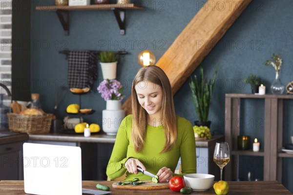 Happy female smiling and cutting cucumber for healthy vegetable salad while watching recipe on