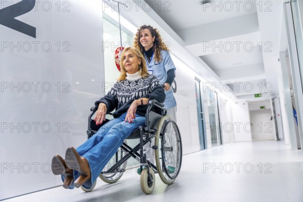 Nurse smiling while pushing a wheelchair with a injured woman along the corridor of the hospital