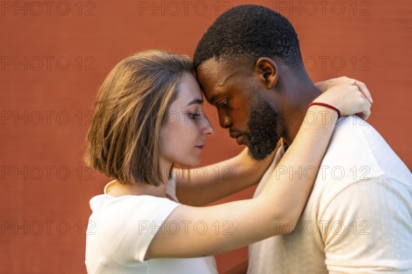 Close-up side view of multi-ethnic lovers embracing against red wall