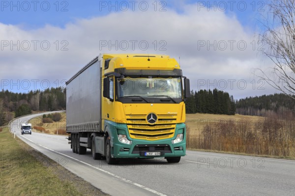 Yellow and green Mercedes-Benz Actros 1845 truck pulls curtainside semi trailer along highway on a