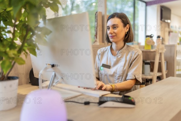 Young female pharmacist using computer sitting in the counter of a modern pharmacy store