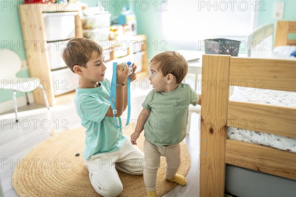 Male little photographer taking a photo of a his baby boy brother in the bedroom
