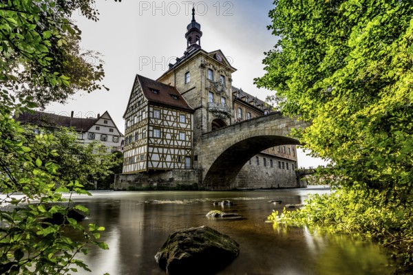 Idyllic half-timbered house on a bridge over a river surrounded by lush greenery and clouds in the
