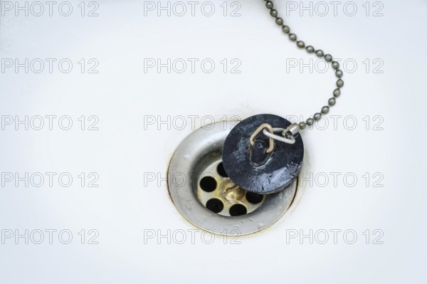 Old black rubber plug with metal chain on a rusty drain in a white wash basin or bathtub, copy