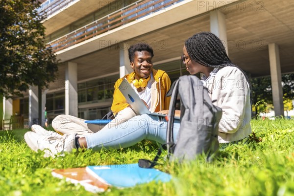 African american students studying with laptop together sitting in the grass outside the campus