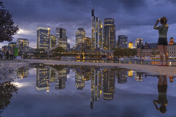 Clouds pass over the glowing Frankfurt bank skyline reflected in a puddle in the evening, Mainufer,