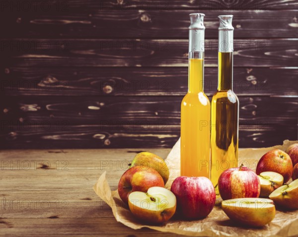 Apple juice with apple vinegar in bottles and fresh apples on wooden background