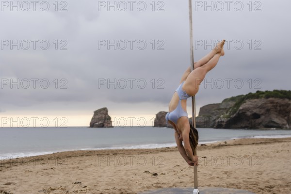 Acrobatics of Pole Dance on the sand of Hendaya beach, France. A young man helping the other to