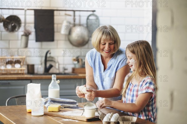 Happy adult mature woman cooking together with cute little girl at table in kitchen