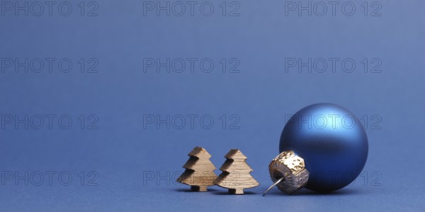 Blue Christmas tree ball with small wooden tree shapes on a blue paper background with space for