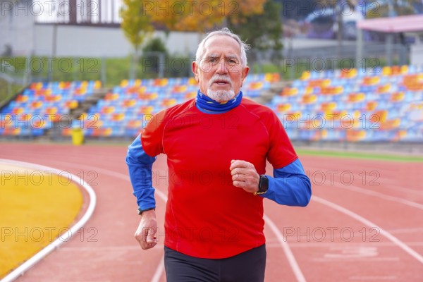 Frontal view portrait of an old man doing en effort running in an athletic track