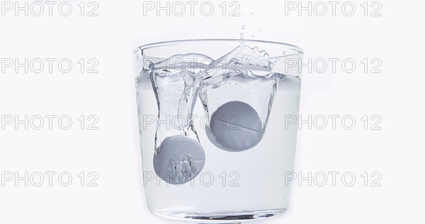 Tablets Falling and Dissolving into a Glass of Water against White Background