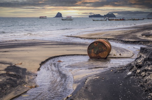 Rusty barrel oil on a partly black coloured beach illustrates the pollution of environment by oil