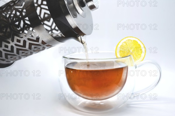 Glass teapot pouring black tea into cup isolated on the white